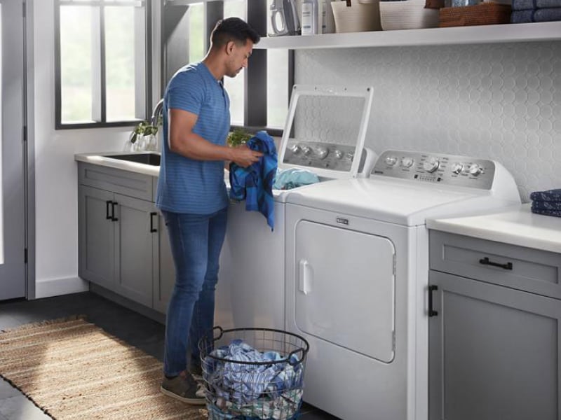 Person placing clothes into a top load washing machine Person placing clothes into a top load washing machine
