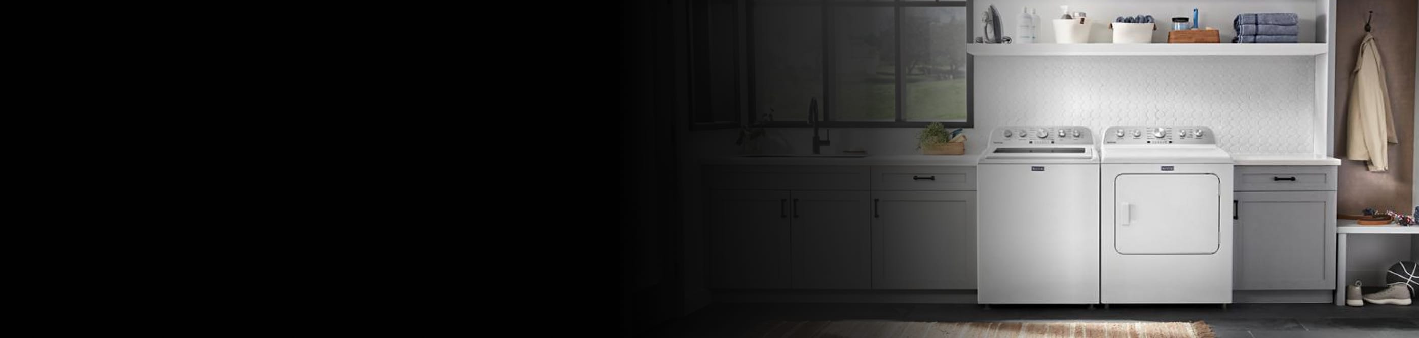 Overview of a laundry room with a top load washer, front load dryer, gray cabinets, and white backsplash tile.