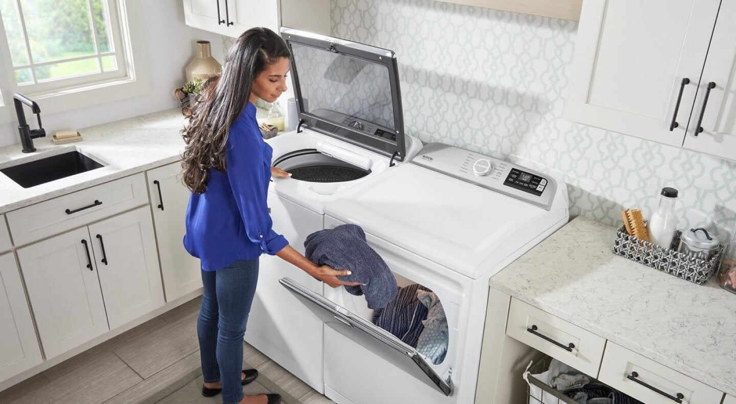 A woman loading washed laundry into a dryer A woman loading washed laundry into a dryer