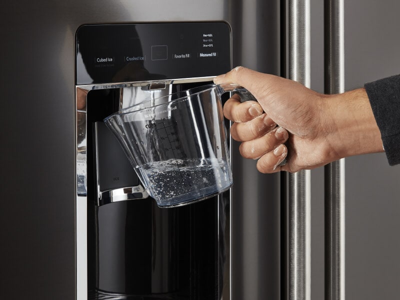 Person filling a large container with water from their refrigerator Person filling a large container with water from their refrigerator
