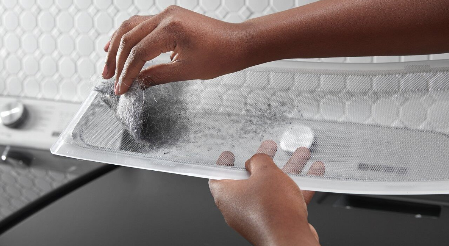 A hand removing lint from the trap A hand removing lint from the trap