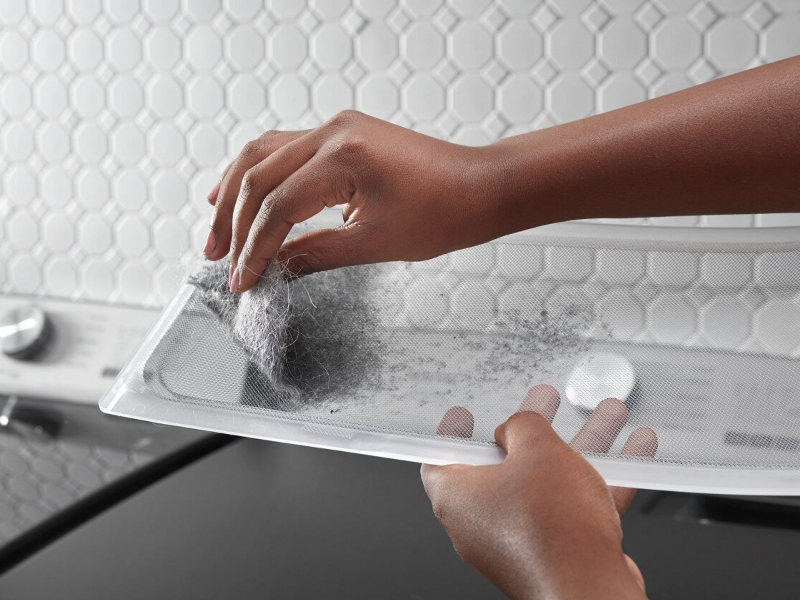 A hand removing lint from the trap A hand removing lint from the trap