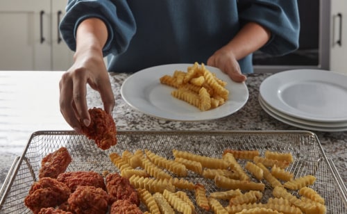 Person transferring chicken and fries from air fry basket to plate