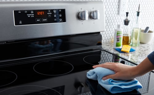 Person wiping down a glass Maytag® cooktop