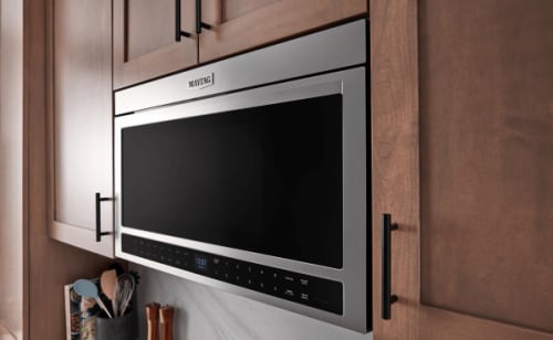 A Maytag® over-the-range built-in microwave surrounded by brown upper cabinets