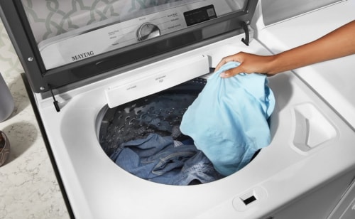 A person adding laundry to a Maytag® washer