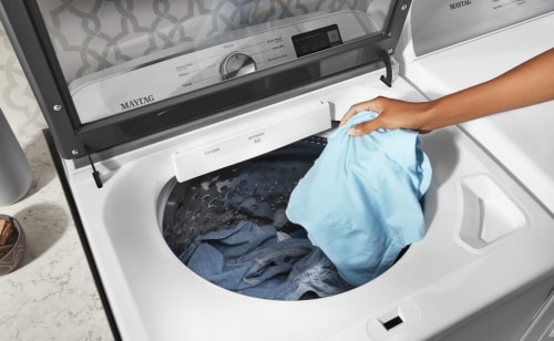 Person putting a blue shirt into a washing machine