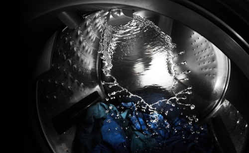 Blue and green clothing tumbling in a washer full of water