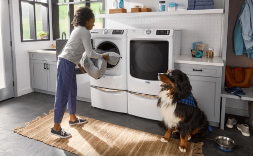 A person taking a pet bed out of a Maytag® front load washer in a laundry room