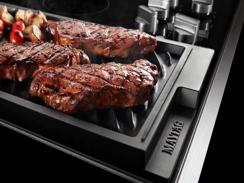 Steak and vegetables cooking on a stovetop griddle